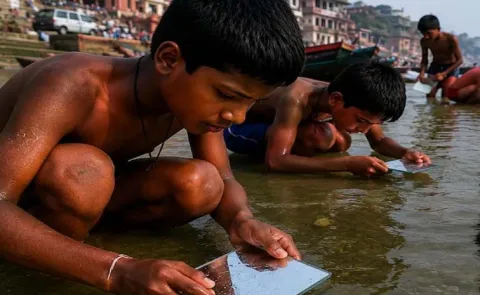 People Searching Gold And Silver Coins In Ganga River Banks With Glass